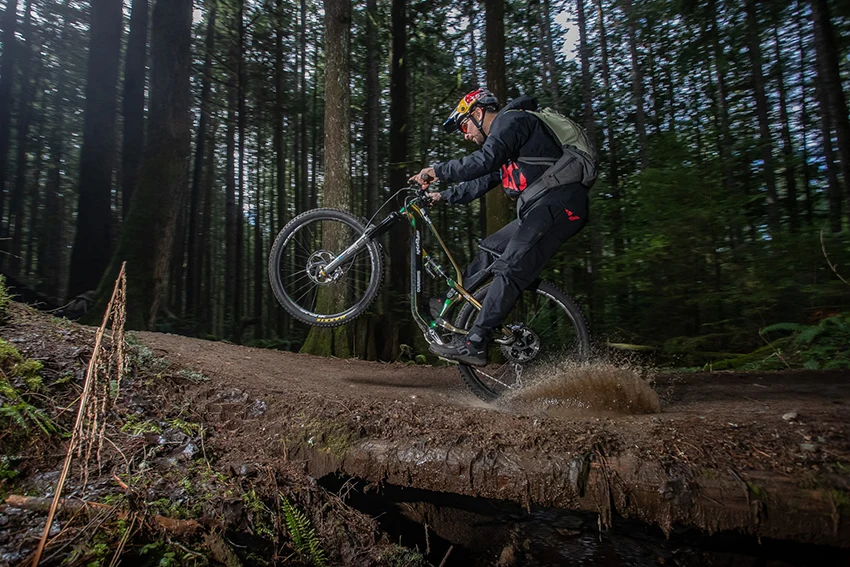 mountain biker doing a wheelie in the forest while wearing mountain biking shoes