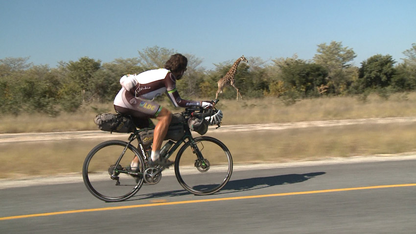 mark riding alongside a giraffe in africa