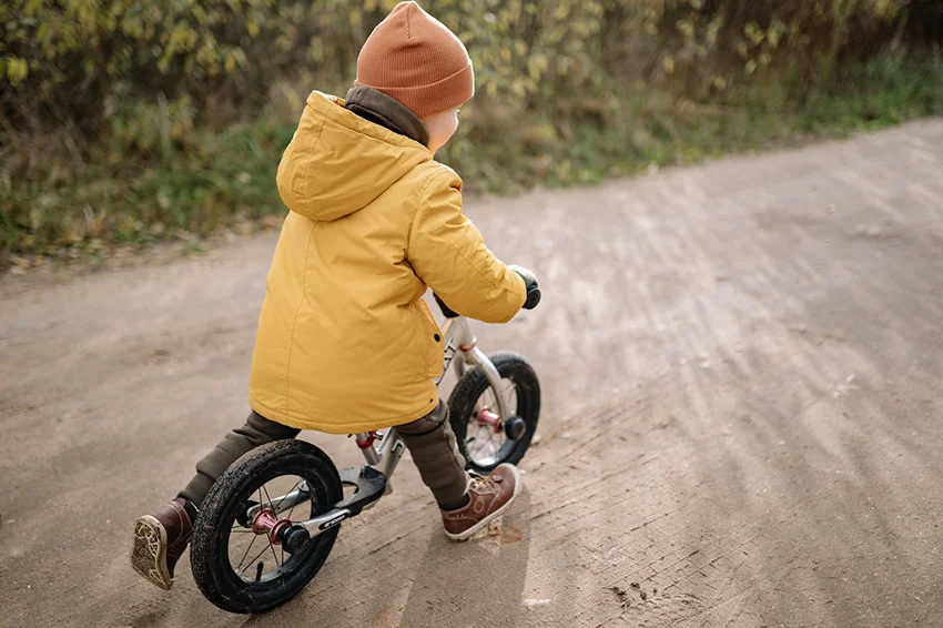 child in yellow jacked riding a kids bike