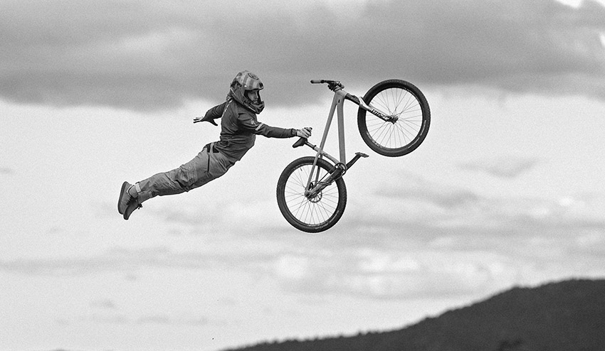 a black and white image of a man in mid-air doing a jump on a specialized dirt jump mountain bike