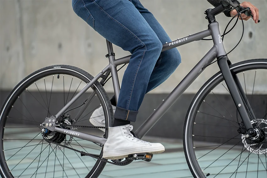 a closeup of a gray priority bicycle and a rider wearing jeans on it